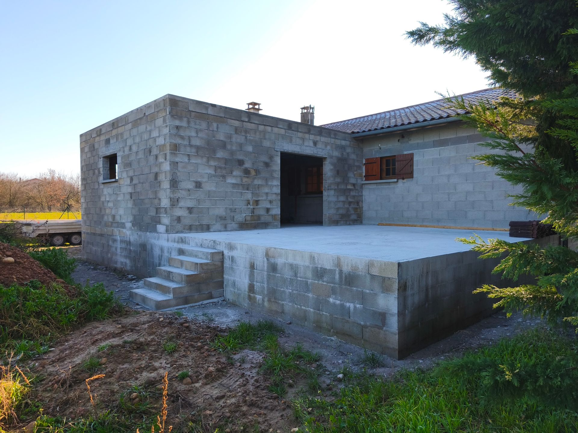 Extérieur d'un bâtiment en parpaings en construction, avec une terrasse et des escaliers.
