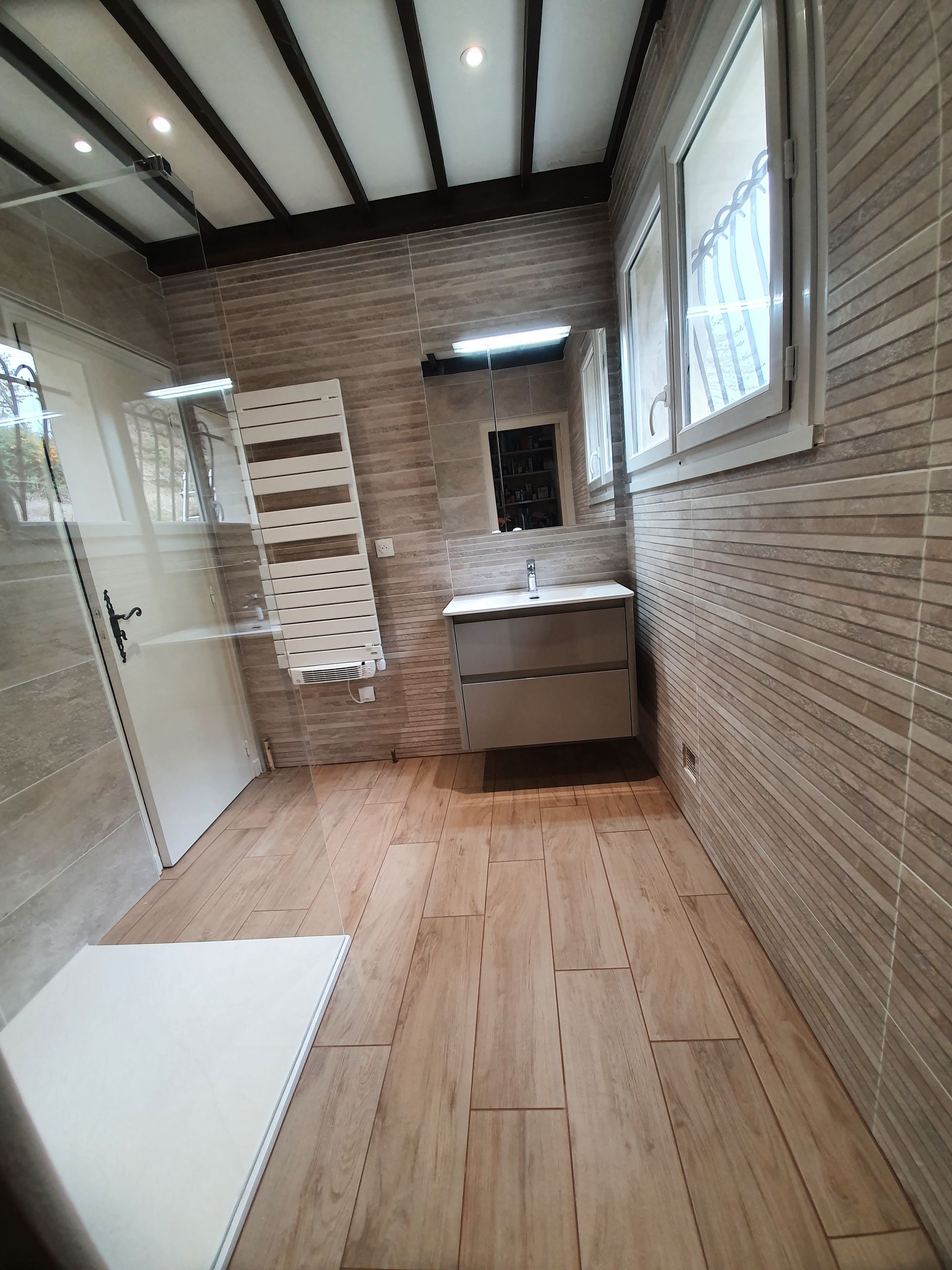 Une salle de bains comprenant une douche, une vasque avec son meuble, un sèche-serviettes