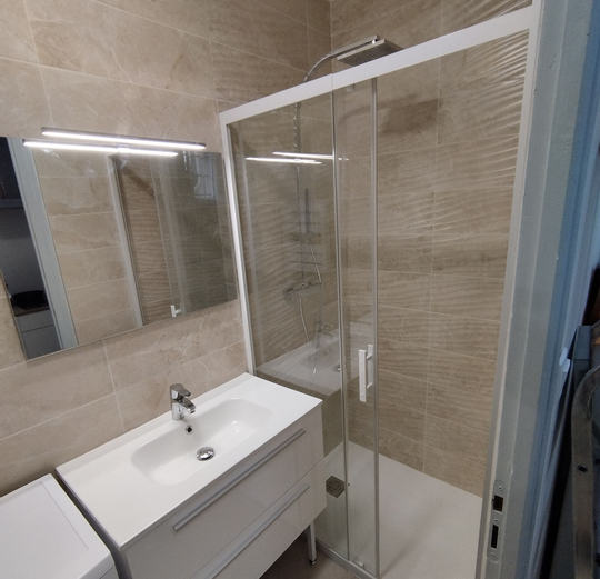 Des murs en carrelage dans une salle de bains comprenant une douche et une vasque dans un meuble
