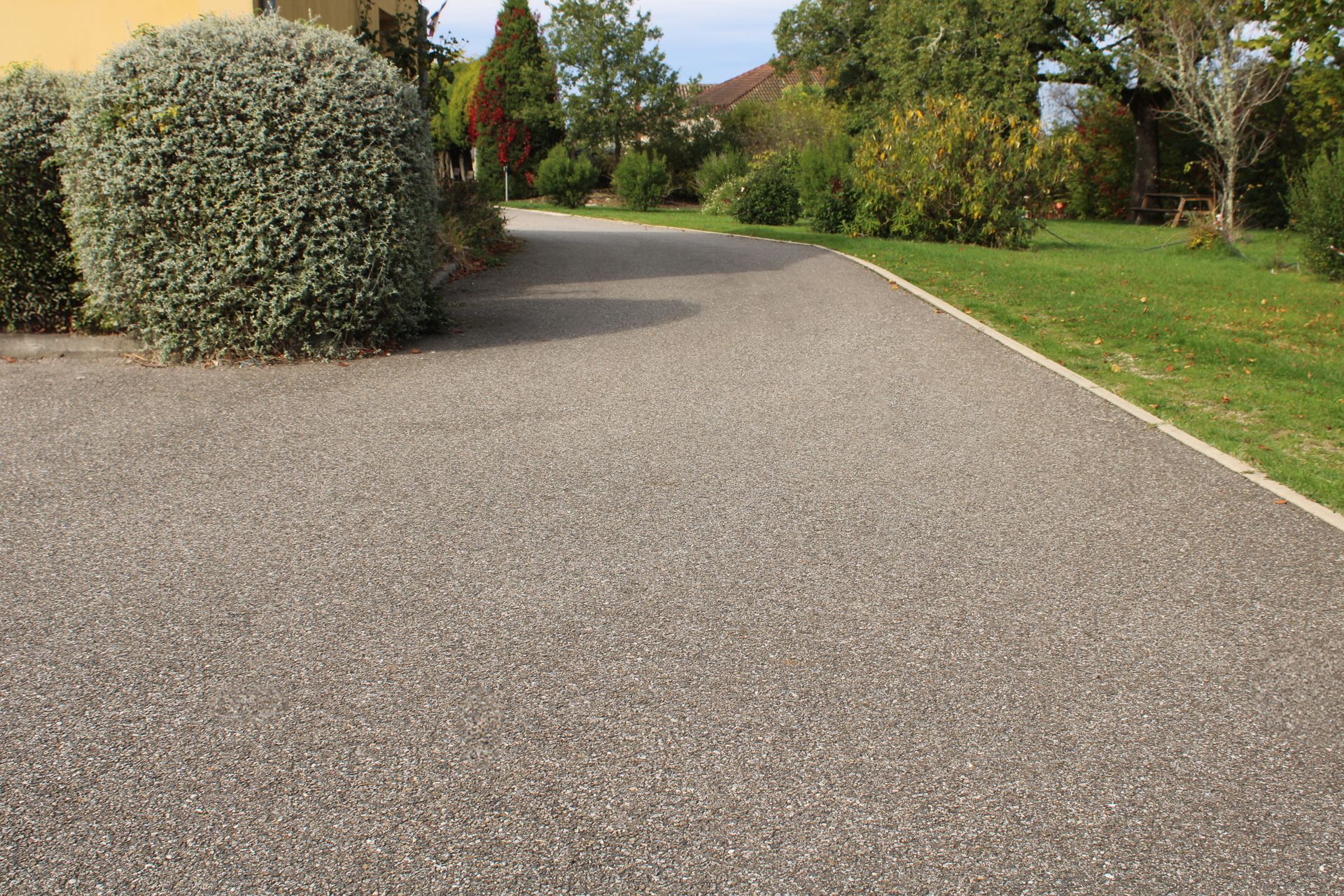 Allée de jardin en gravier serpentant à travers un aménagement paysager verdoyant, agrémenté de buissons taillés et de pelouses.