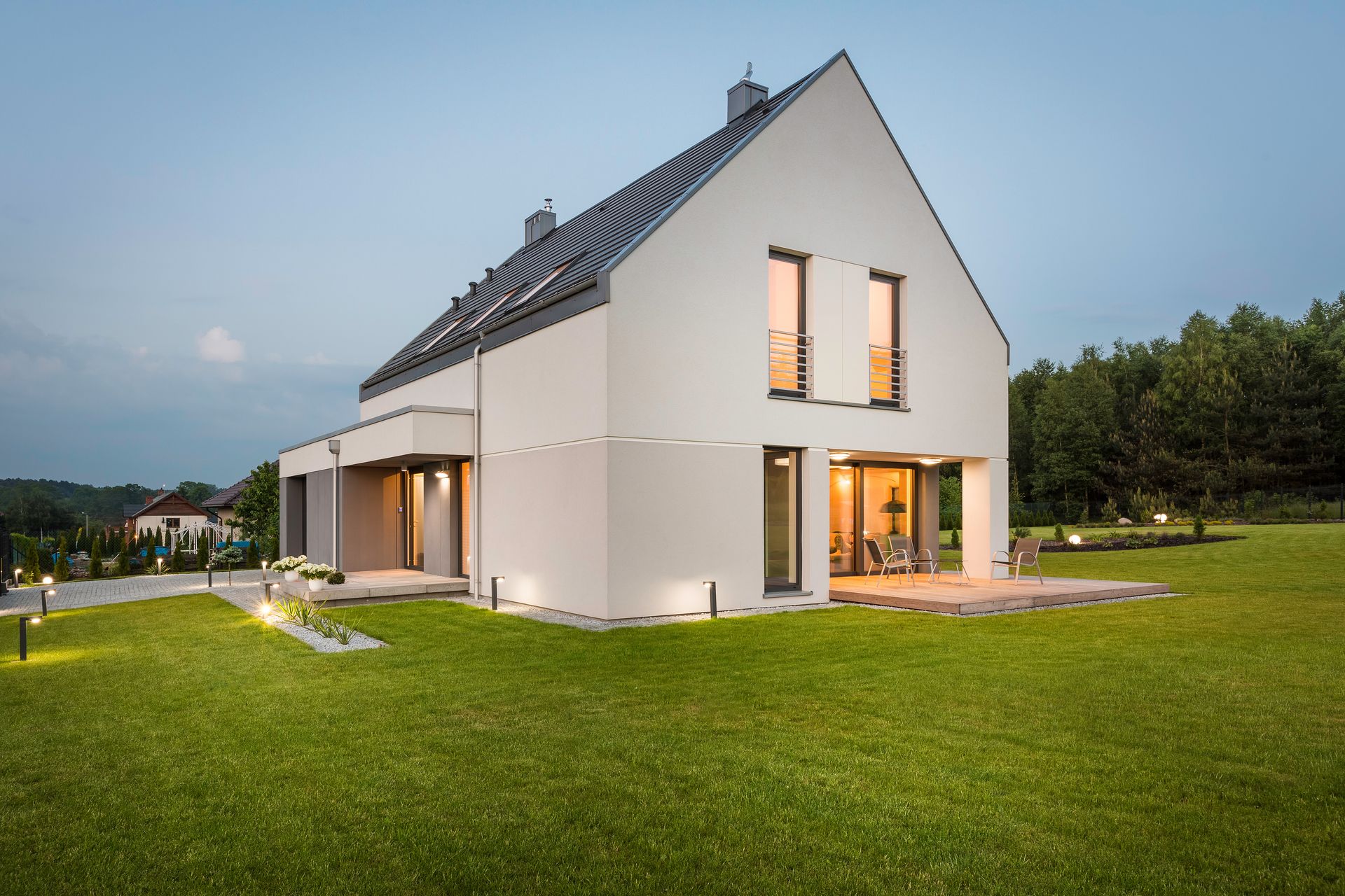 Maison moderne avec un toit en pente et des fenêtres éclairées, entourée d'une pelouse verte au crépuscule