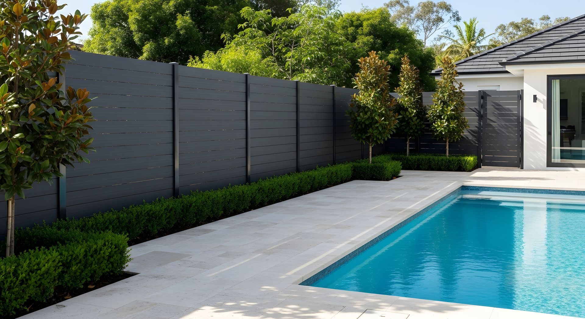 Patio moderne dans une cour arrière avec piscine, mur gris et verdure à côté d'une maison
