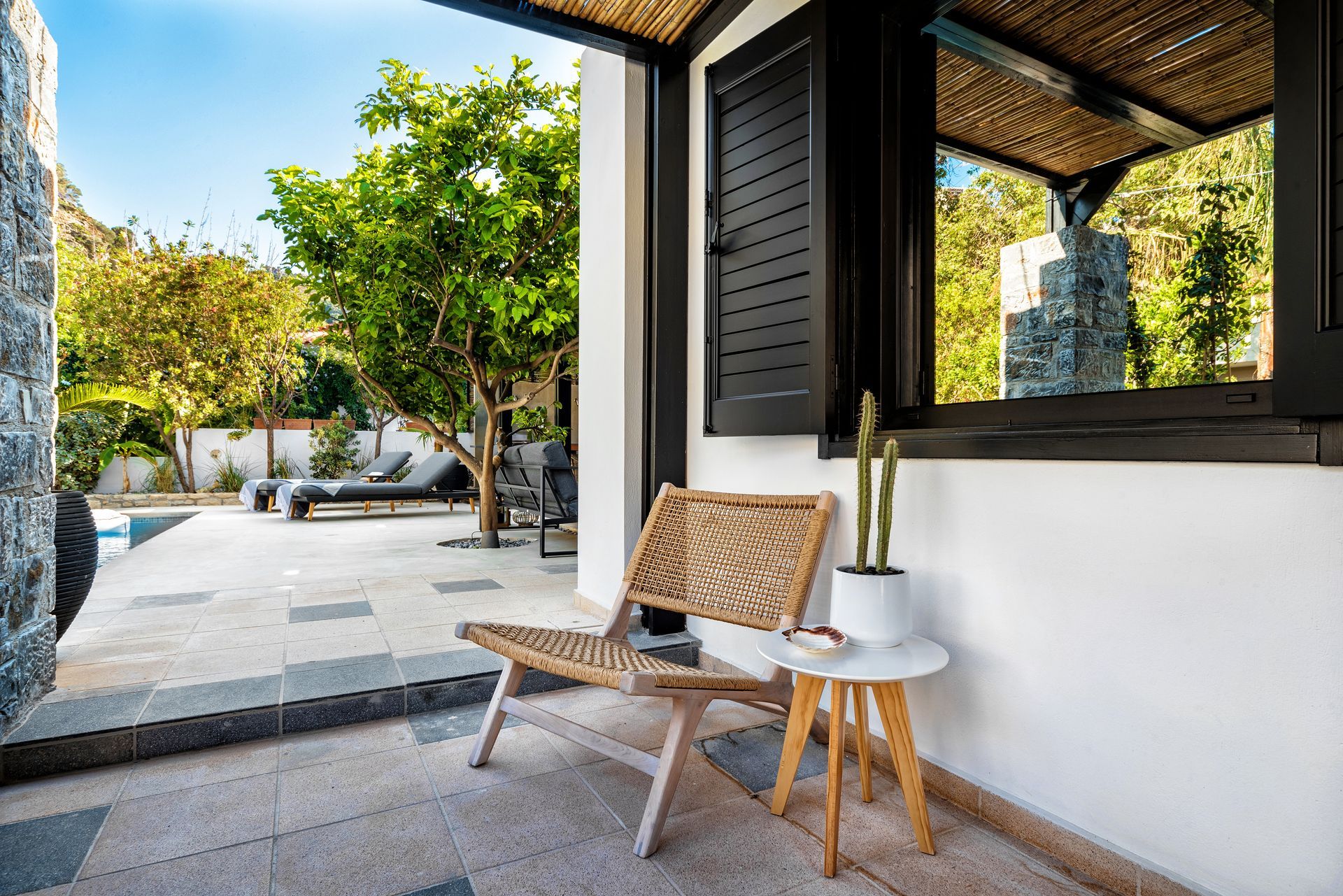 Patio moderne avec chaise en osier, petite table et plante en pot près d'une fenêtre de maison