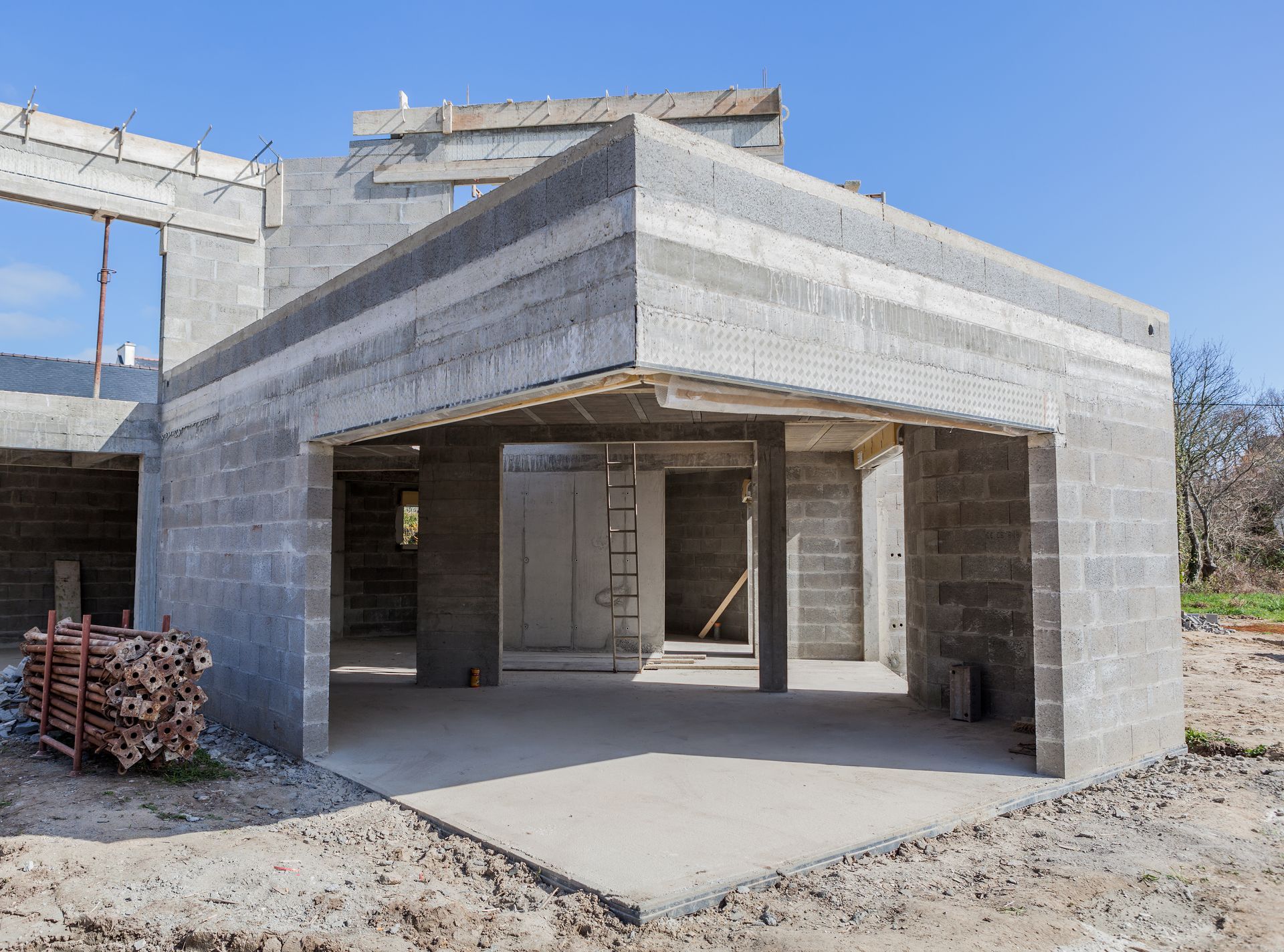 Bâtiment en béton en construction avec entrée ouverte de type garage et toit inachevé sur un terrain en terre battue