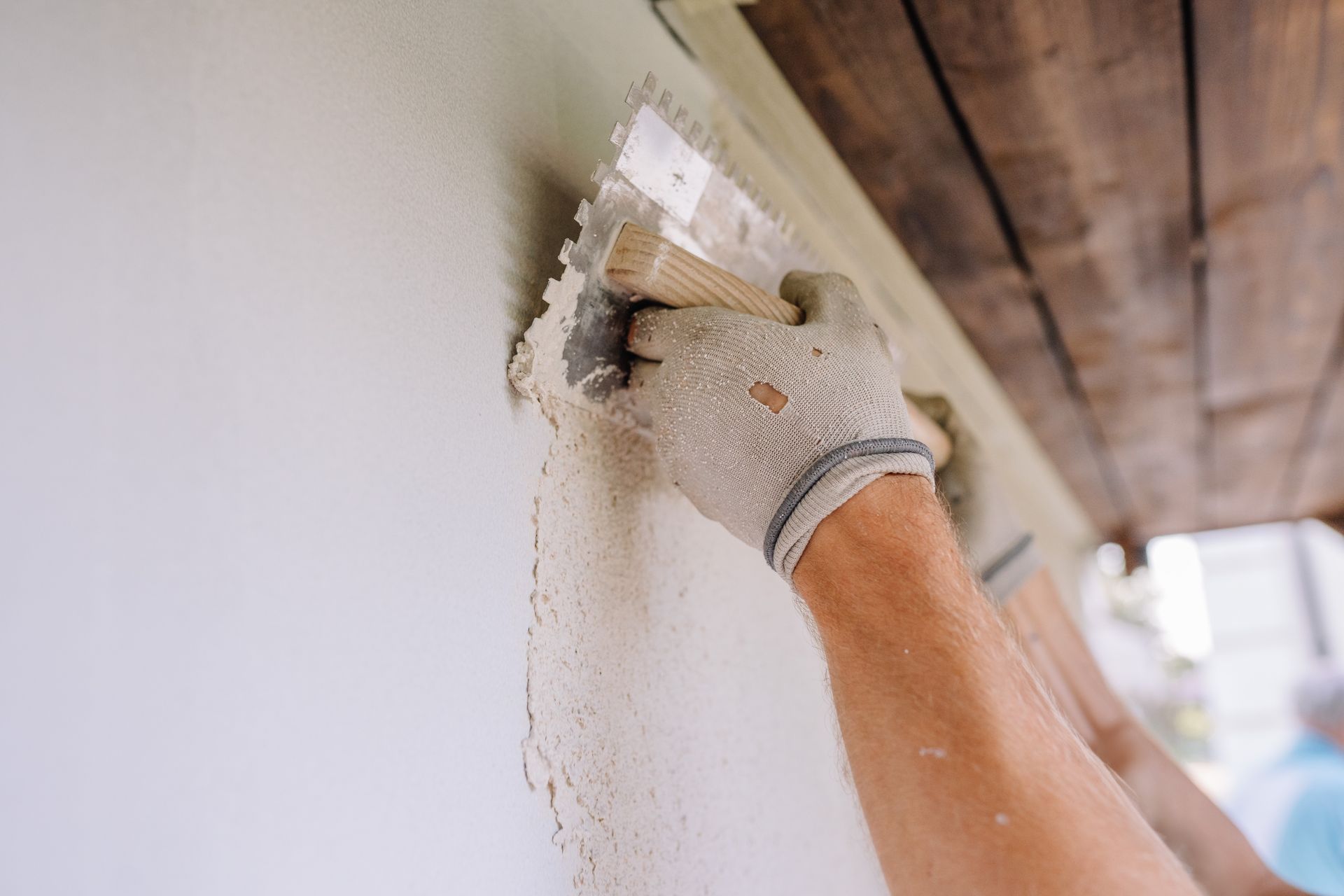 Main gantée appliquant du plâtre sur un mur à l'aide d'une truelle à l'intérieur