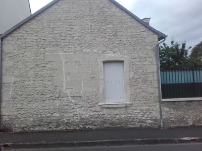 Mur en pierre d'une maison avec une petite fenêtre à volets blancs donnant sur une rue