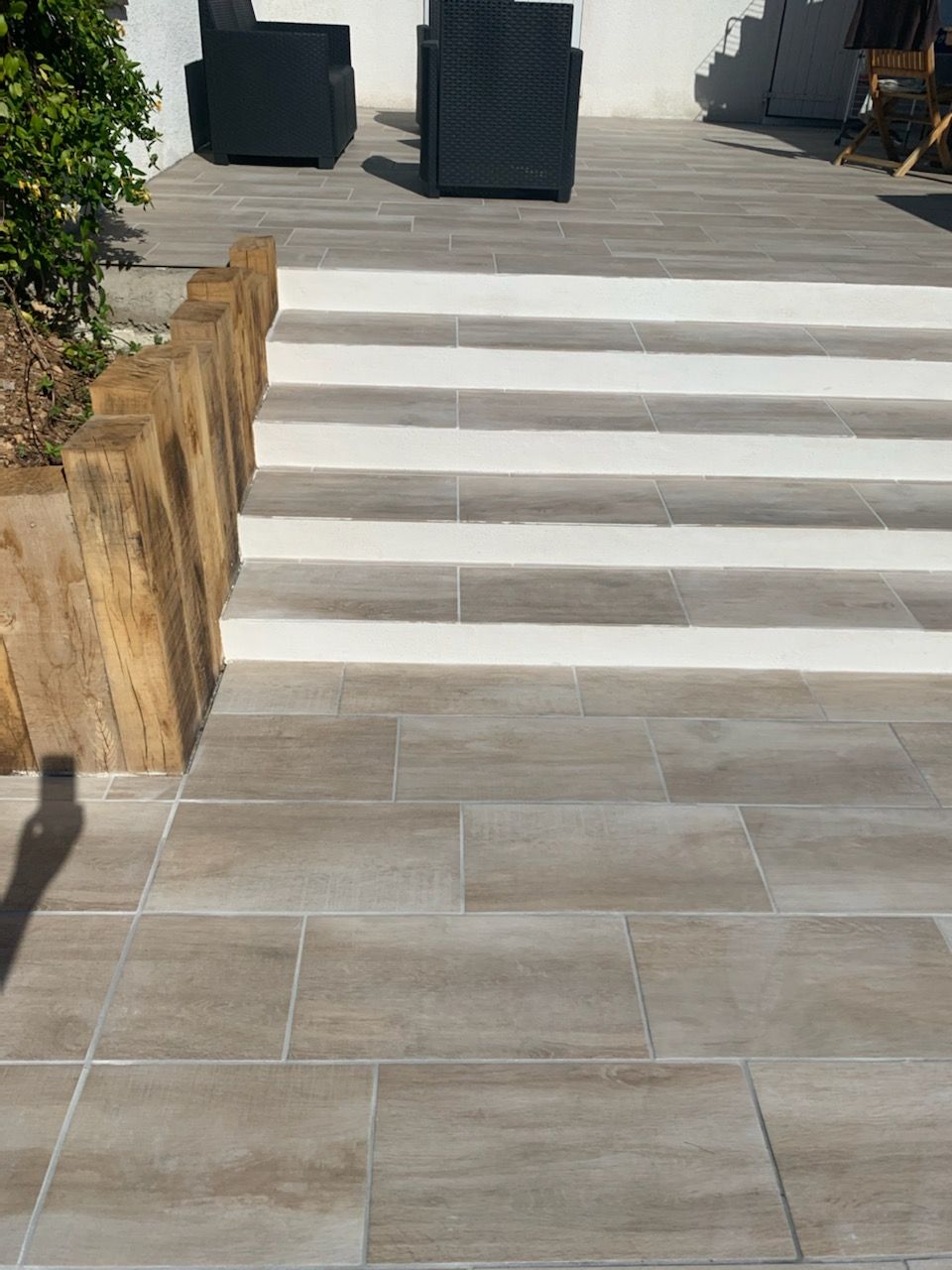 Escaliers extérieurs avec contremarches blanches, dalles de pierre grise et chaises noires sur une terrasse ensoleillée