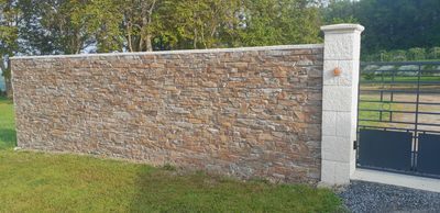Un mur de pierre avec un pilier blanc à côté d'un portail en métal noir.