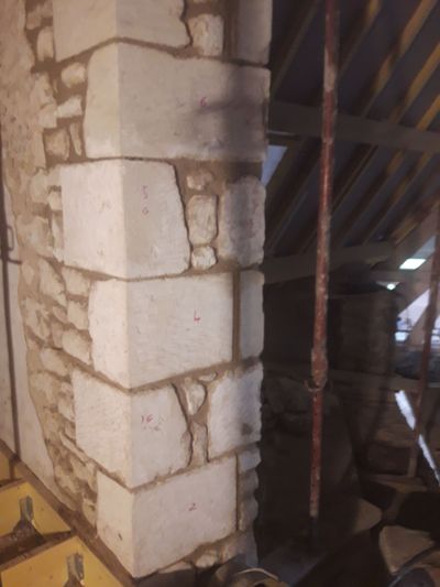 Mur et colonne en pierre dans un grenier, avec des poutres en bois apparentes