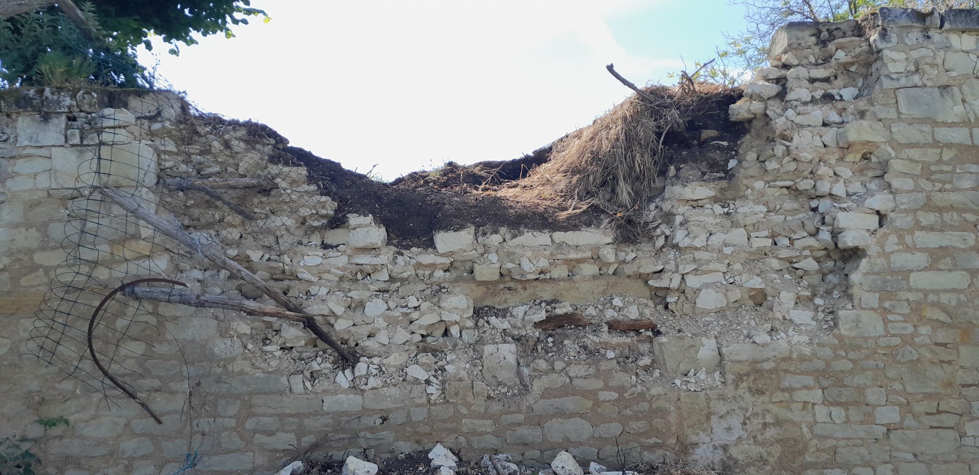 Mur de pierre en ruine, partie supérieure effondrée et recouverte de végétation