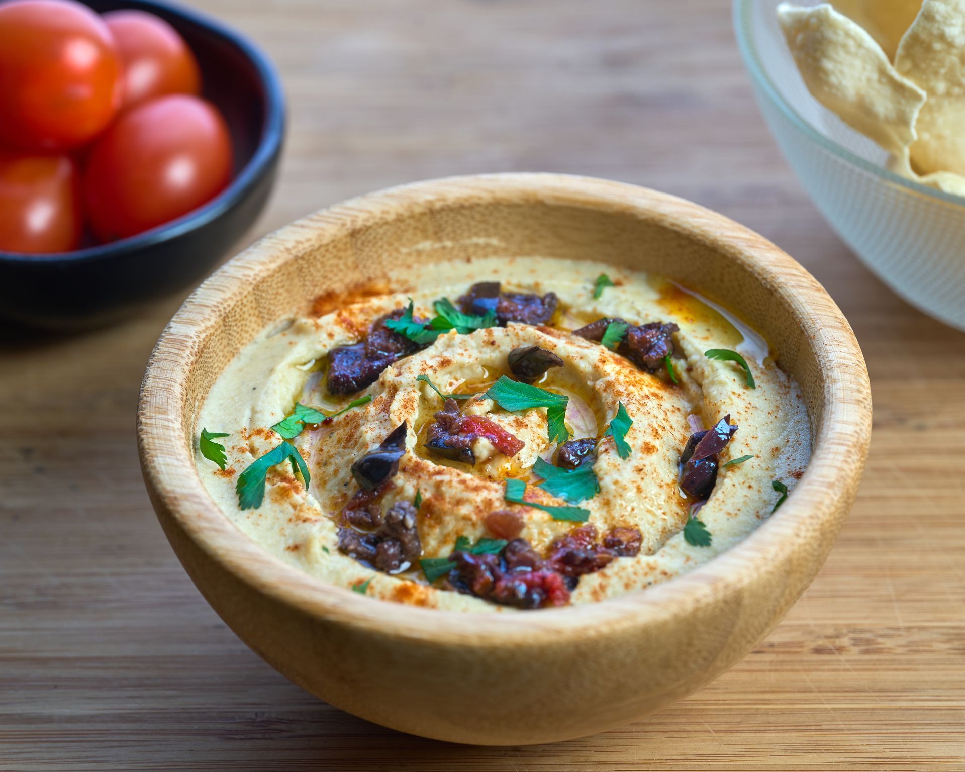 Hummus en cuenco de madera con pimentón y aceite de oliva, servido con tomates y patatas fritas.