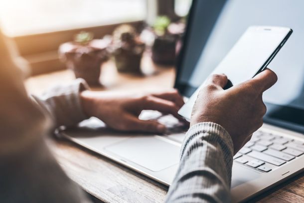 Des mains tapant sur un ordinateur portable tout en tenant un Smartphone à un bureau.