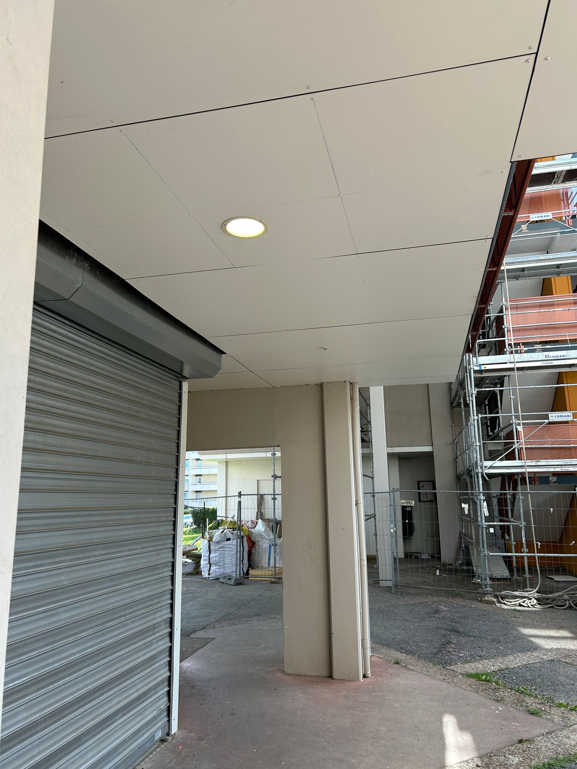 Allée extérieure couverte avec un volet métallique fermé et des échafaudages à côté d'un bâtiment.