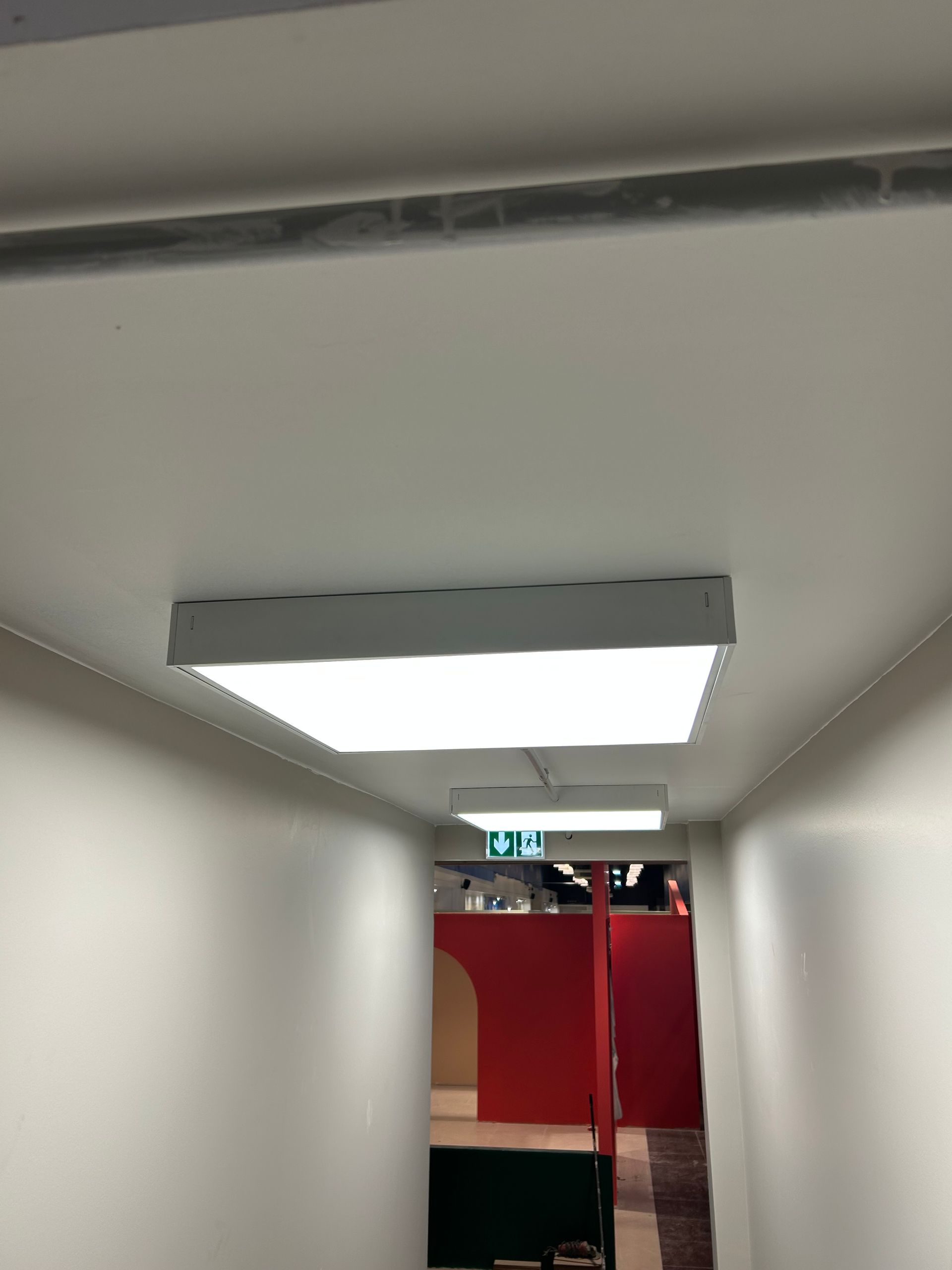 Couloir étroit avec un plafonnier et une cloison rouge au fond, vu de l'intérieur d'un bâtiment.