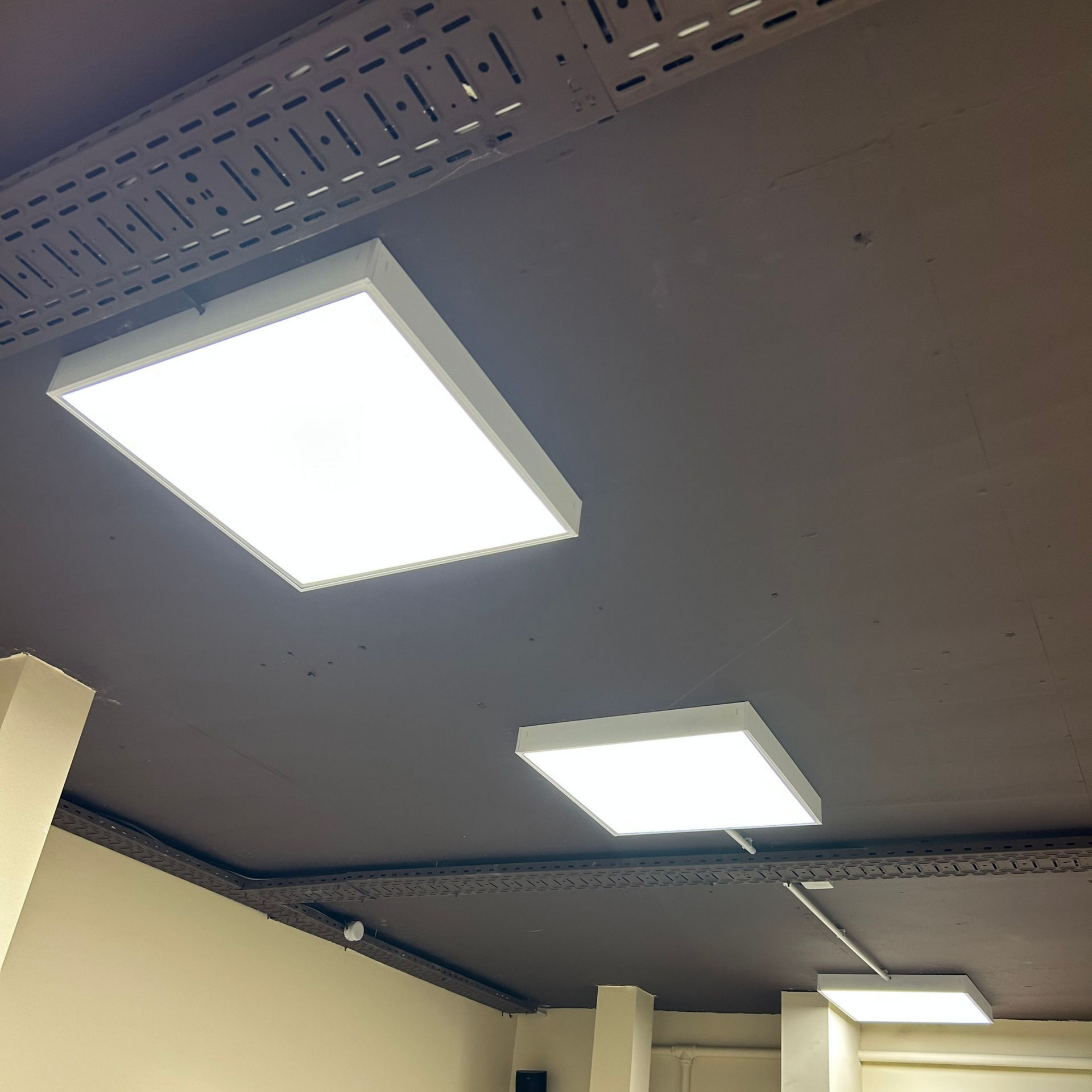 Plafond avec trois panneaux lumineux fluorescents carrés dans une pièce beige.