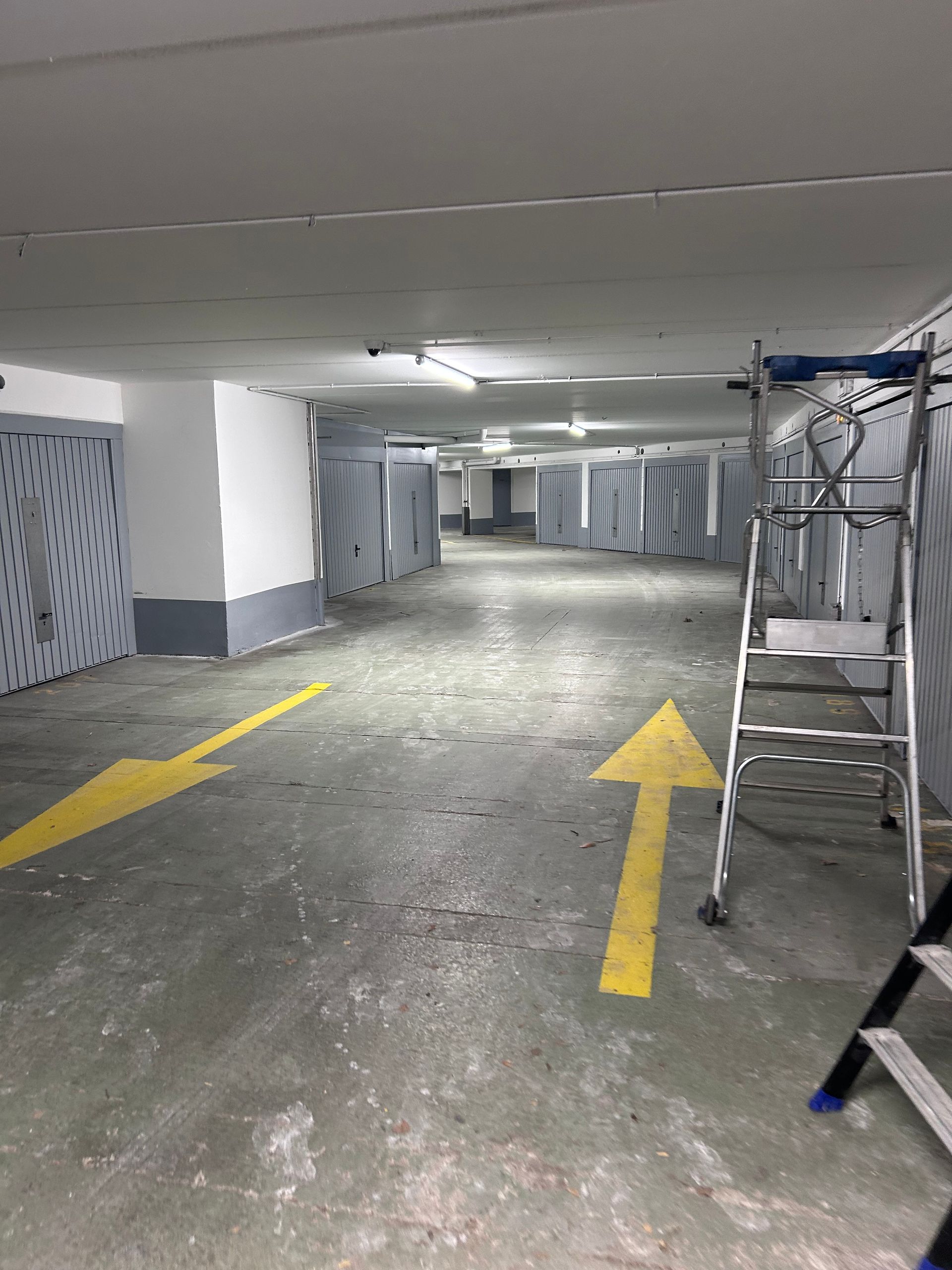 Parking souterrain avec flèches directionnelles jaunes et une échelle sur le côté droit.