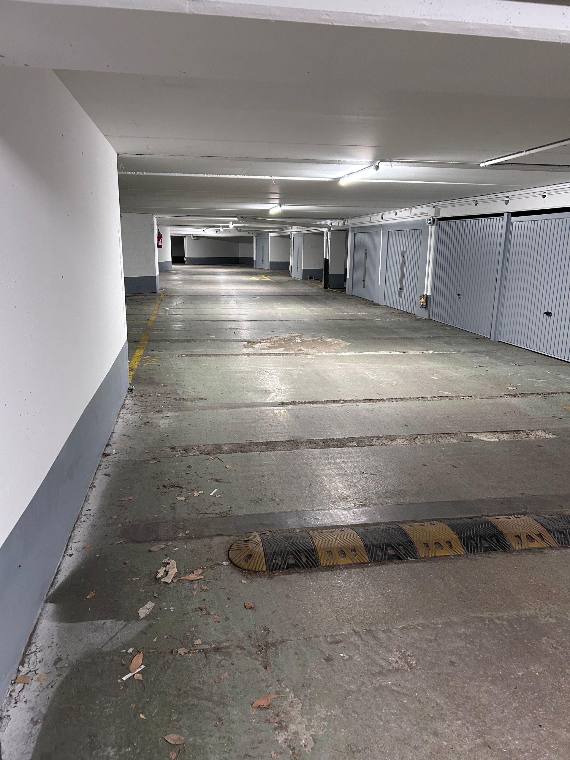 Parking souterrain vide aux murs blancs et ralentisseurs rayés.