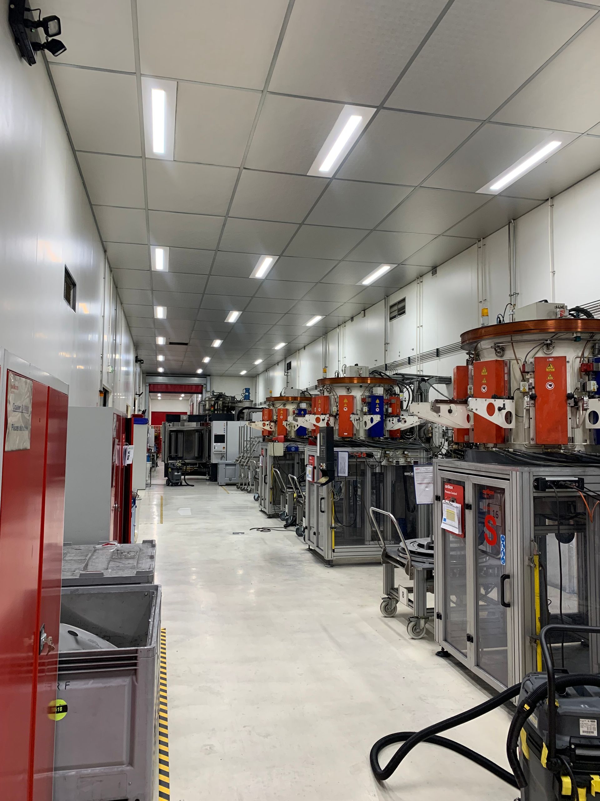Couloir industriel avec sols blancs et éclairage au plafond, bordé de machines et d'équipements orange.