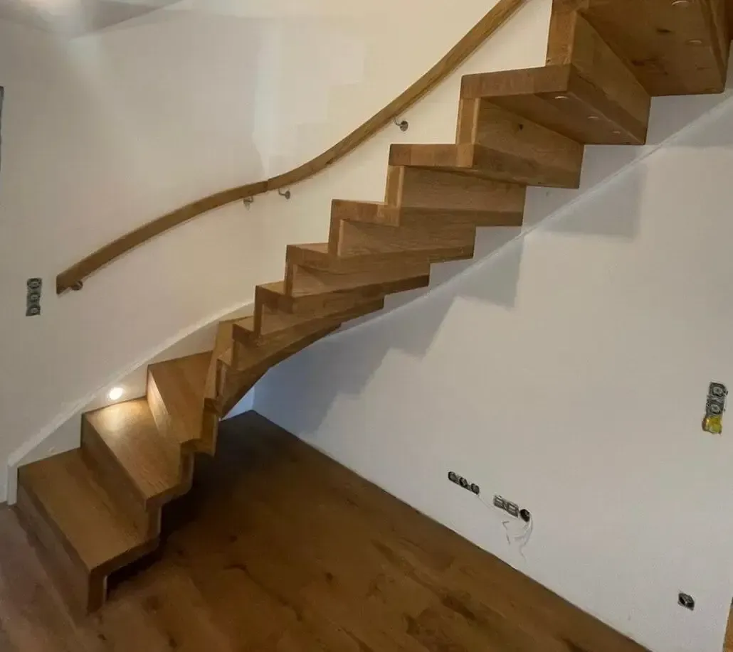 Eine moderne, geschwungene Holztreppe mit integriertem Handlauf und eingelassener Beleuchtung vor einer weißen Wand.