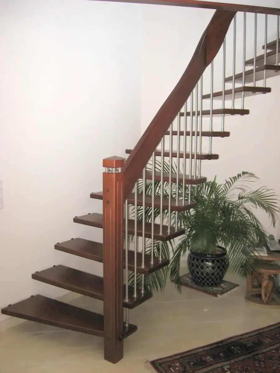 Eine Holztreppe mit offenen Setzstufen, Metallspindeln und einem Handlauf in einem hellen Raum mit einer Topfpflanze.