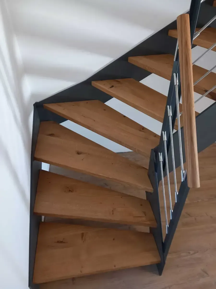 Eine moderne Treppe mit Holzstufen und einem dunklen Metallrahmen und -geländer, von oben betrachtet.