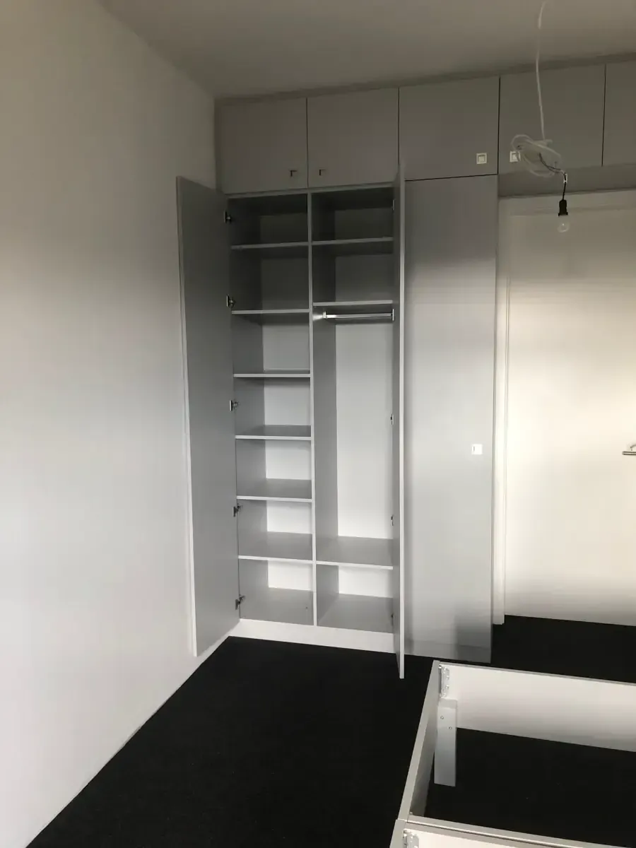 Ein grauer Kleiderschrank mit offenen Türen gibt den Blick auf Regalböden und eine Kleiderstange frei