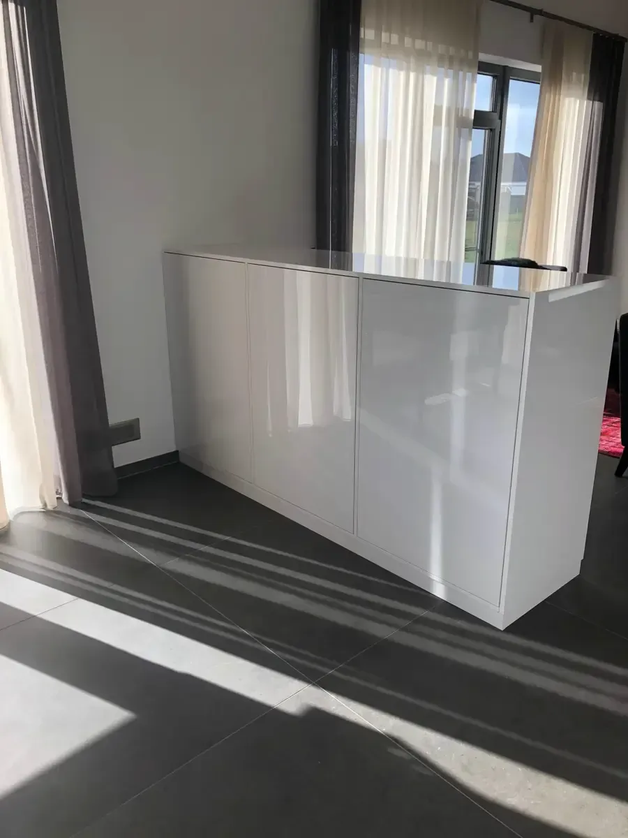 In einem Raum mit lichtdurchlässigen Vorhängen steht ein glänzend weißer, rechteckiger Schrank