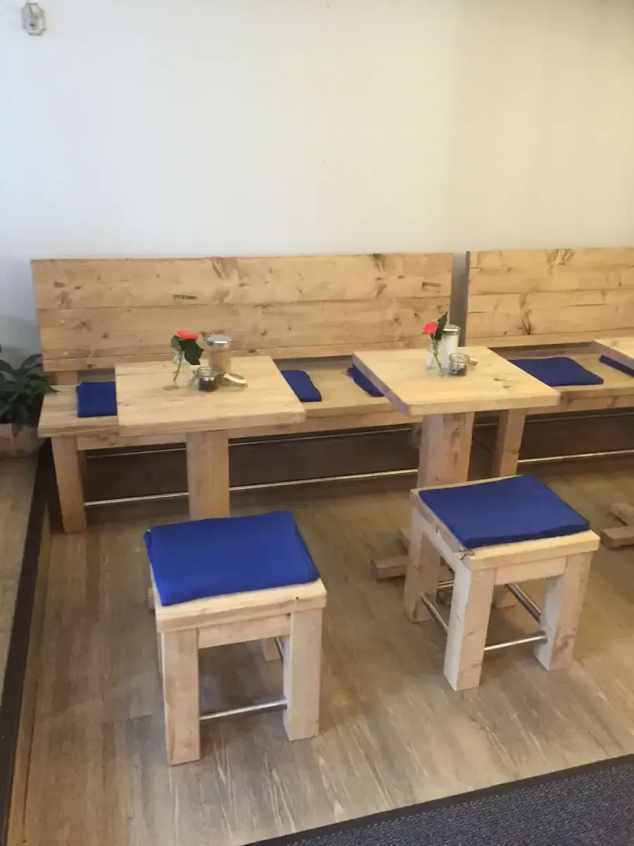 Zwei helle Holztische mit Bänken und Hockern, jeweils mit blauen Sitzkissen