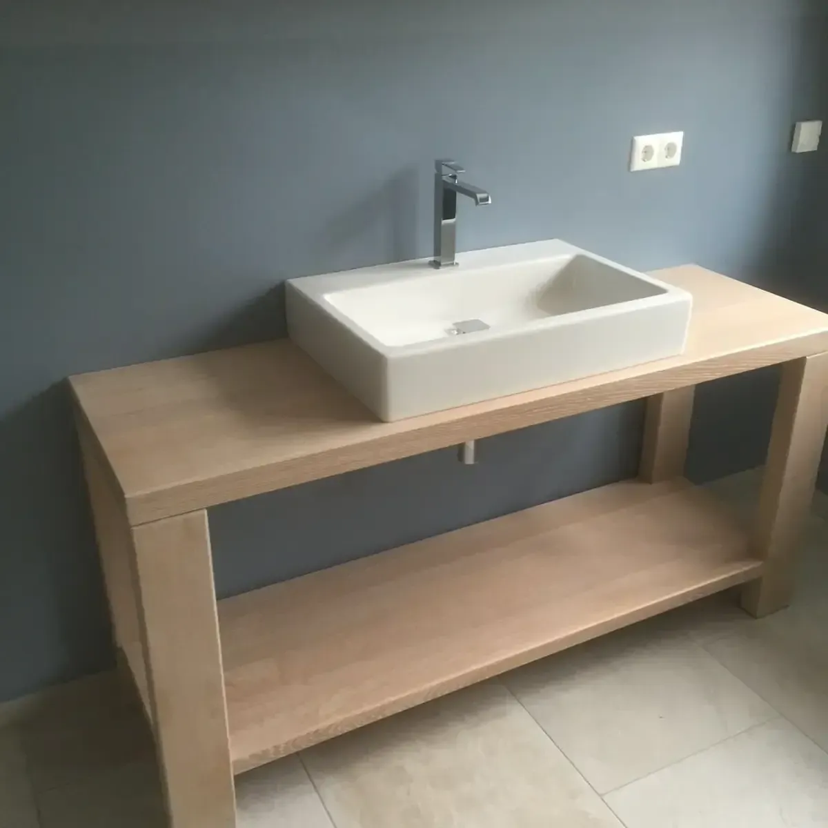 Ein moderner Badezimmerwaschtisch mit rechteckigem, weißem Aufsatzwaschbecken und verchromter Armatur vor einer grauen Wand.