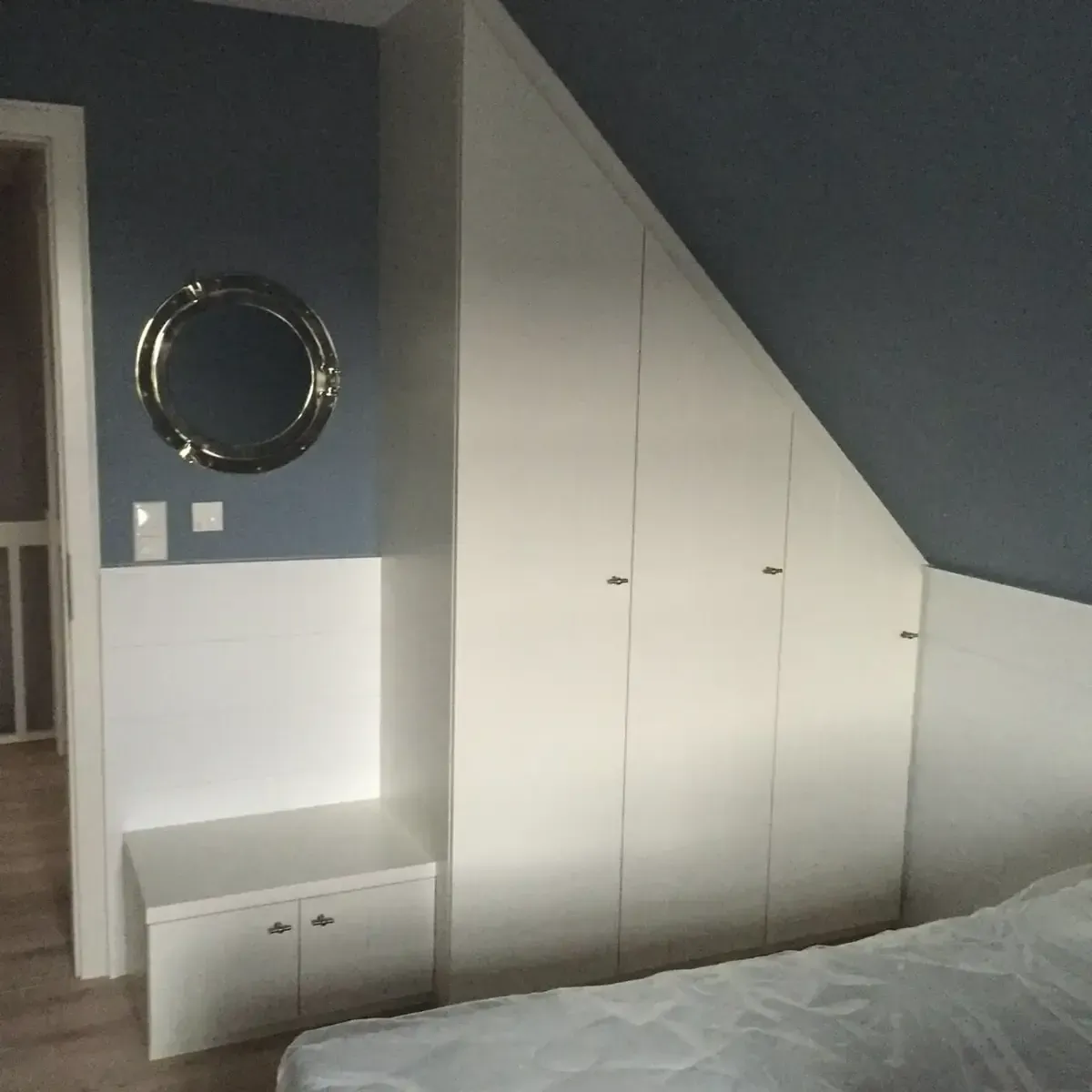 Ein weißer, maßgefertigter, schräger Kleiderschrank und ein dazu passendes niedriges Aufbewahrungsmöbel