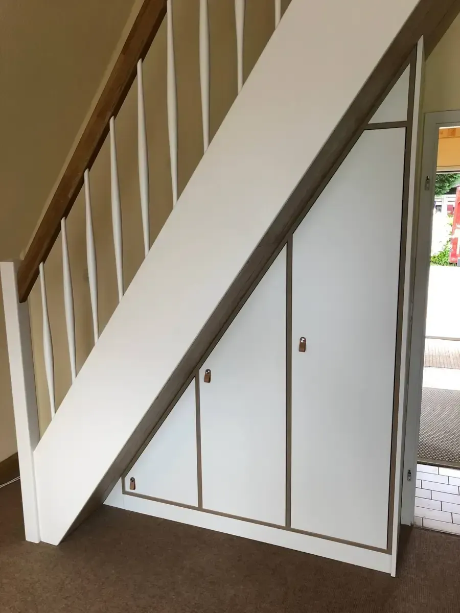 Weiße Unterschrankschränke mit holzfarbenen Zierleisten wurden unter einer Treppe mit Holzgeländer installiert.