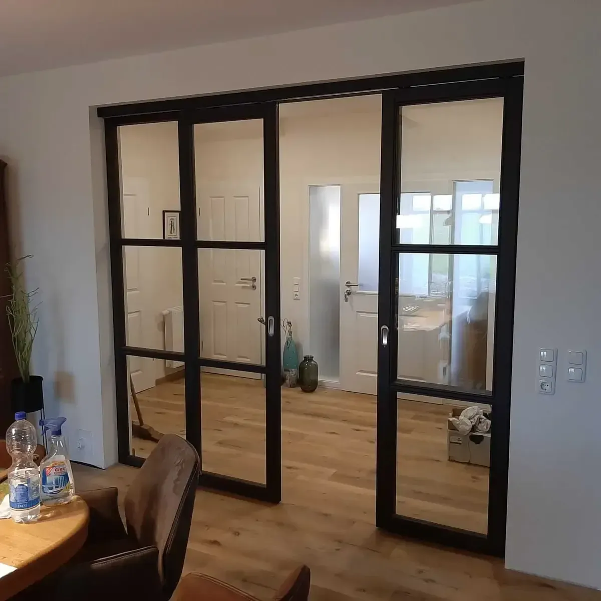 Eine schwarze, mehrteilige Glasschiebetür wurde in einem Haus mit hellem Holzboden und weißen Wänden installiert.