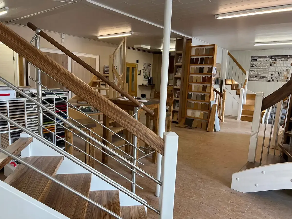 Ein Ausstellungsraum, in dem verschiedene Bodenbelagsmuster, Treppengeländer und Holzmaterialien präsentiert werden.