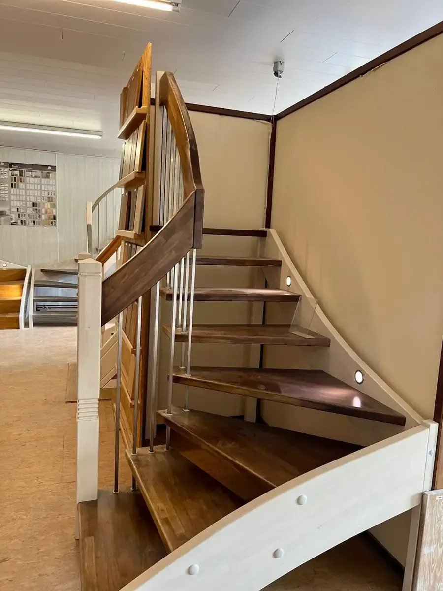 Eine Holztreppe mit weißen Seitenpaneelen und integrierter Stufenbeleuchtung in einem Ausstellungsraum.
