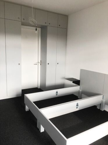Ein weißes Bettgestell und dazu passende, deckenhohe Einbauschränke