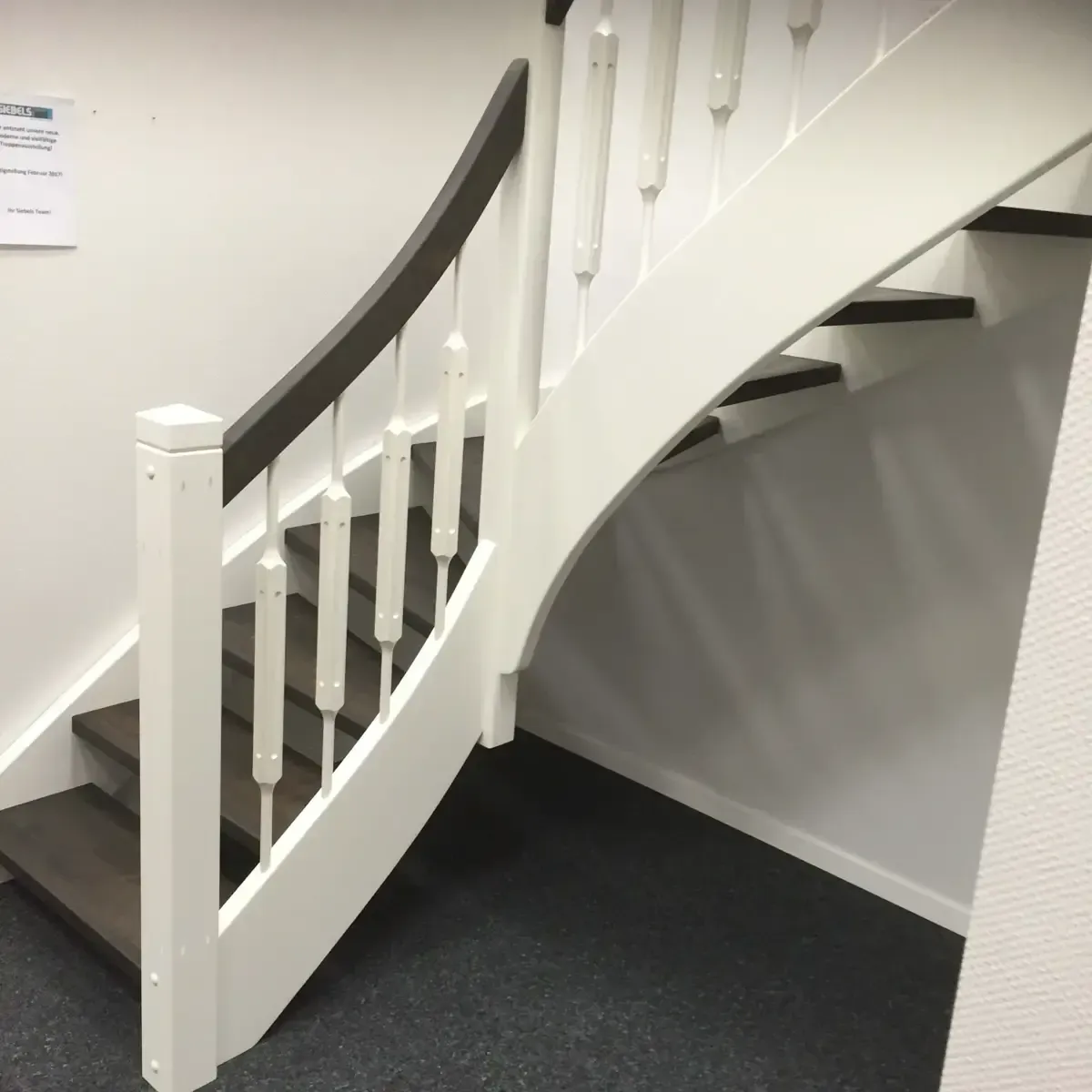 Eine geschwungene Holztreppe mit dunklen Stufen, dunklem Handlauf und weißen Geländern und Zierleisten