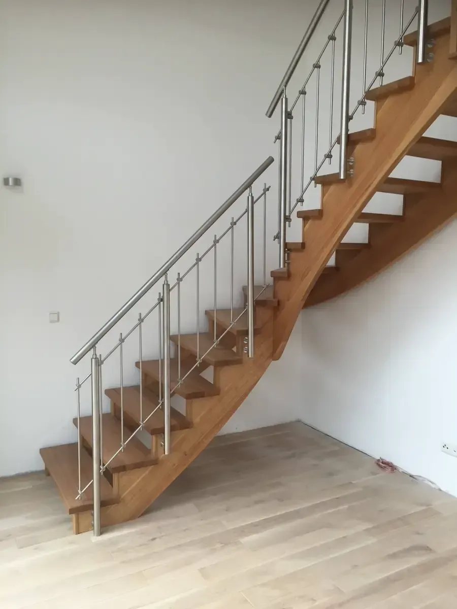 Eine Holztreppe mit Edelstahlgeländer in einem Raum mit weißen Wänden und hellem Holzboden.