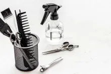Un peine, unas tijeras, una botella de spray y cepillos en una cesta sobre una mesa.