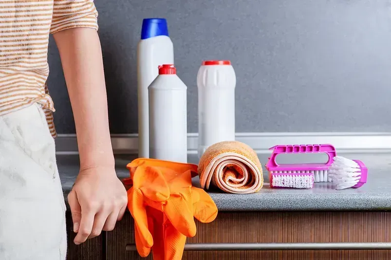 Una persona está parada al lado de un mostrador con productos de limpieza encima.