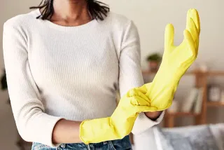 Una mujer se pone guantes de goma amarillos en una sala de estar.