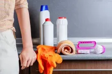 Una persona está parada al lado de un mostrador con productos de limpieza encima.
