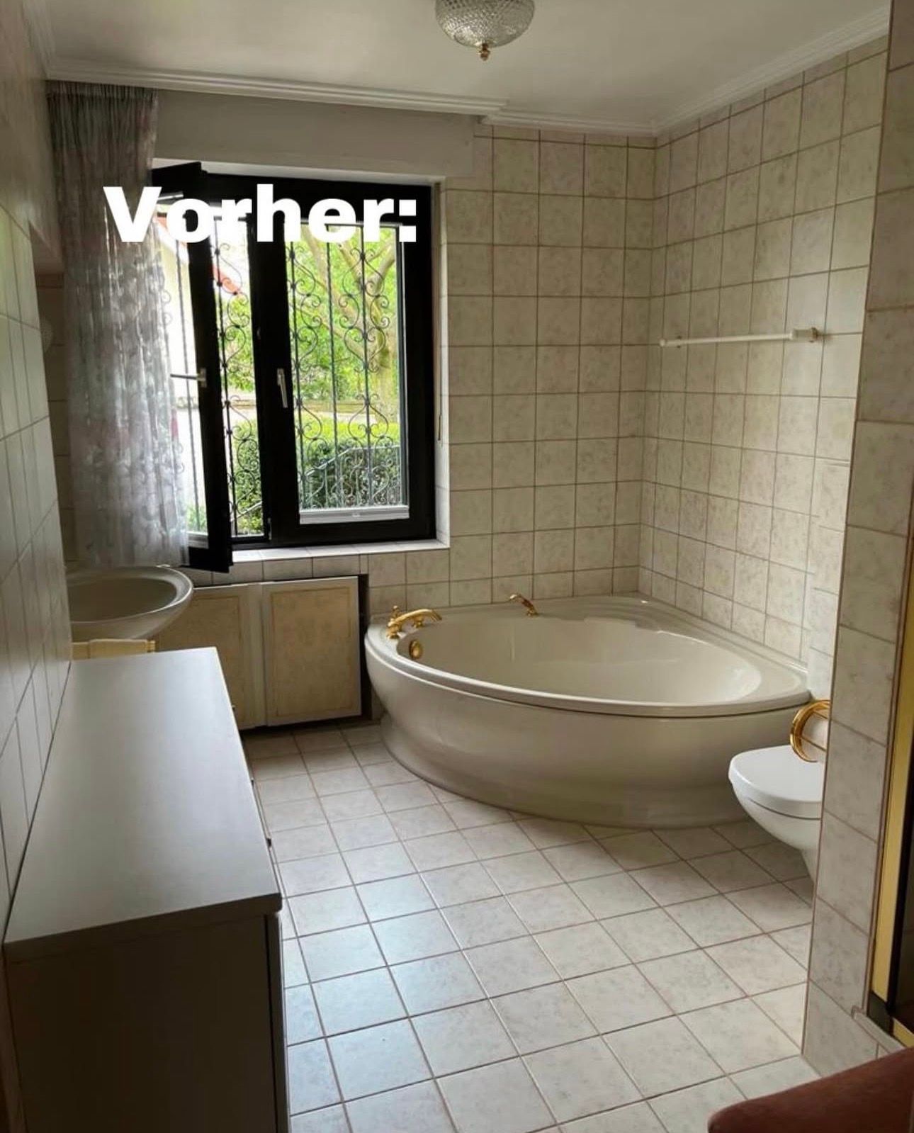 Klassisches Badezimmer mit cremefarbenen Fliesen, ovaler Badewanne, Fenster, Waschbecken und Toilette. Text: 