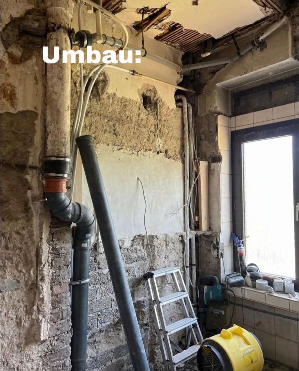 Baustelle: teilweise abgerissener Innenraum mit freiliegenden Rohren und einer kleinen Leiter. Aufschrift: „Umbau“.