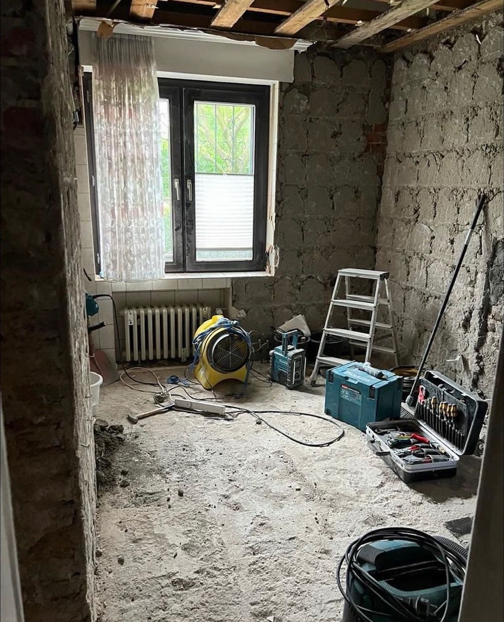 Innenraum im Renovierungszustand; freiliegende Ziegelwände, Werkzeuge, Leiter und Bauschutt auf dem Boden.