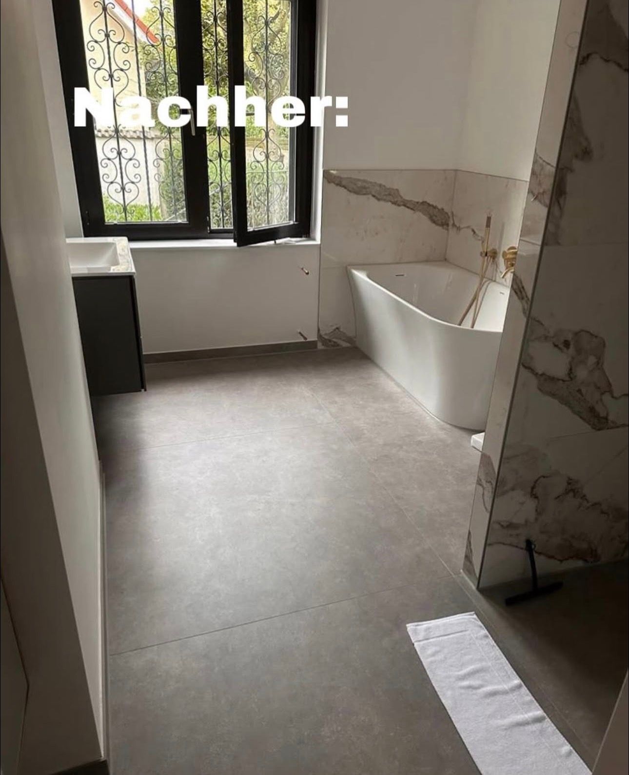 Modernes Badezimmer: weiße Badewanne, grauer Boden, schwarzes Fenster, weiße und marmorne Wandakzente. Text: „Nachher“.