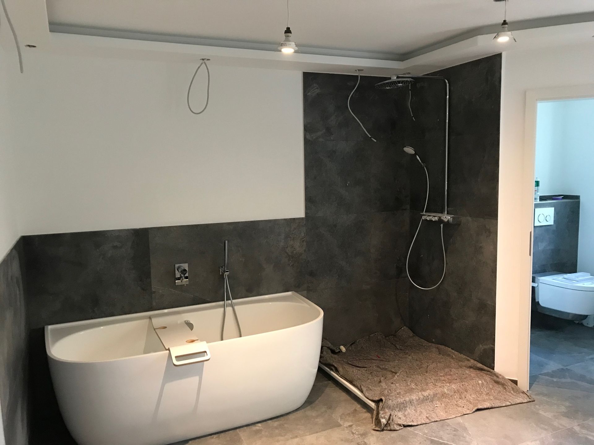 Badezimmer im Bau mit weißer Badewanne, Duschkopf und grauen Fliesenwänden.