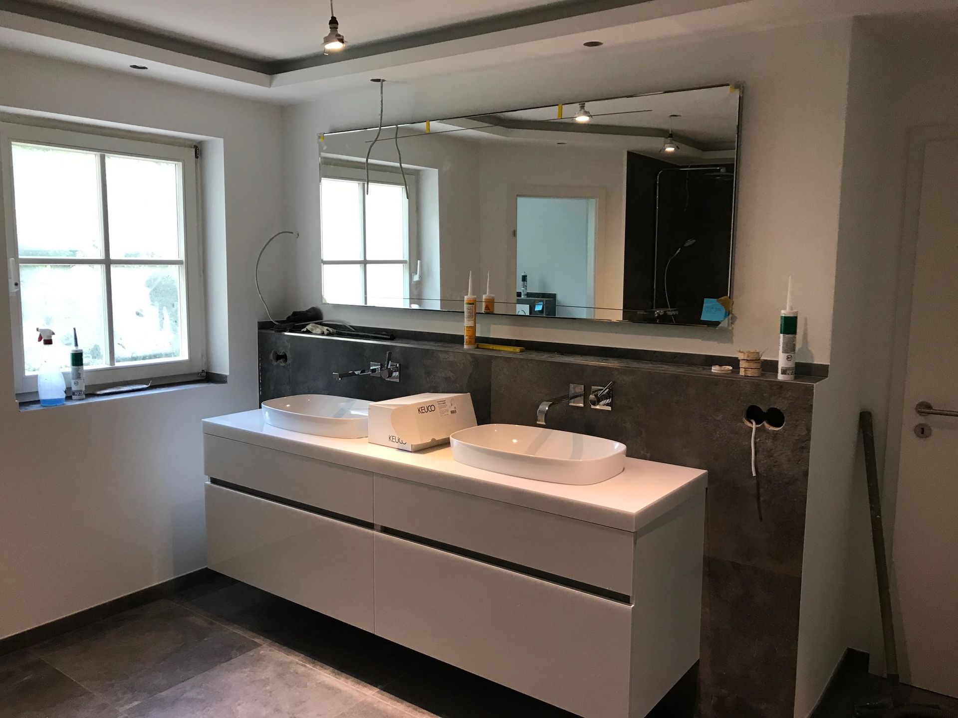 Modernes Badezimmer mit weißem Doppelwaschtisch, großem Spiegel und dunklem Fliesenboden.