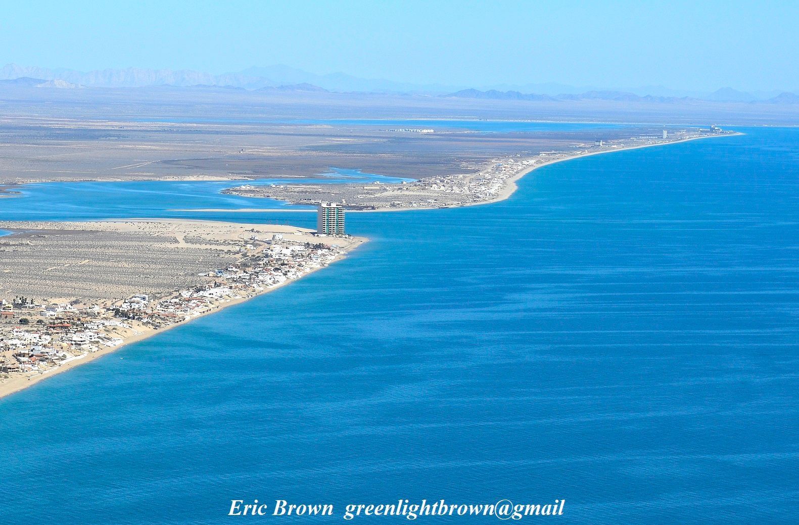 Aerial view of Las Conchas coastline meeting bright blue ocean, with a sprawling city along the shore.