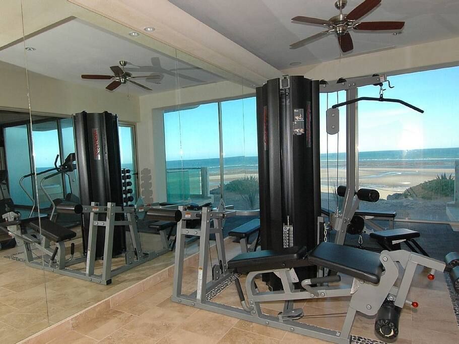 Gym room with exercise machines and large windows overlooking the ocean.