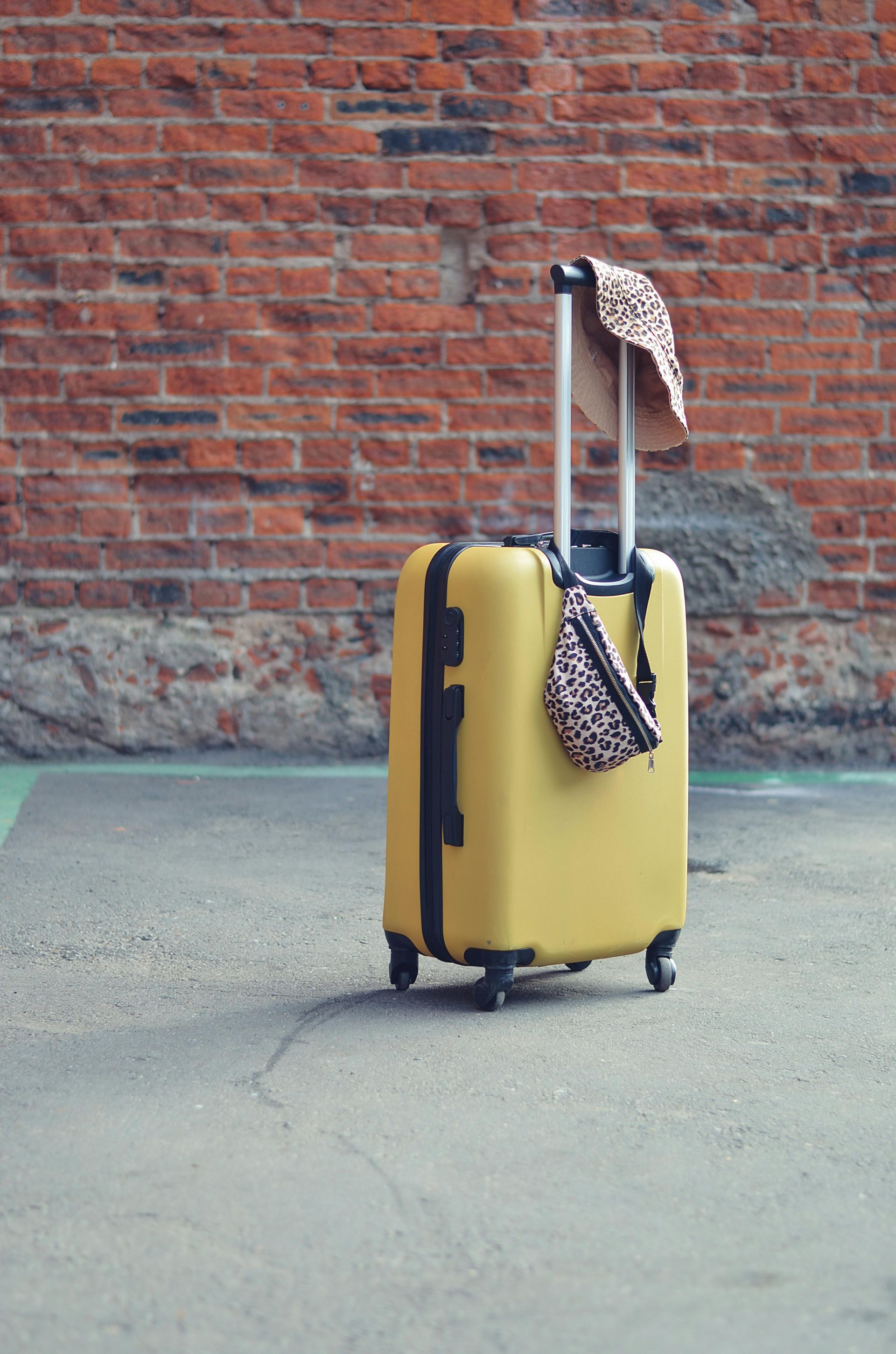 Yellow suitcase with scarf leaning against a brick wall on pavement